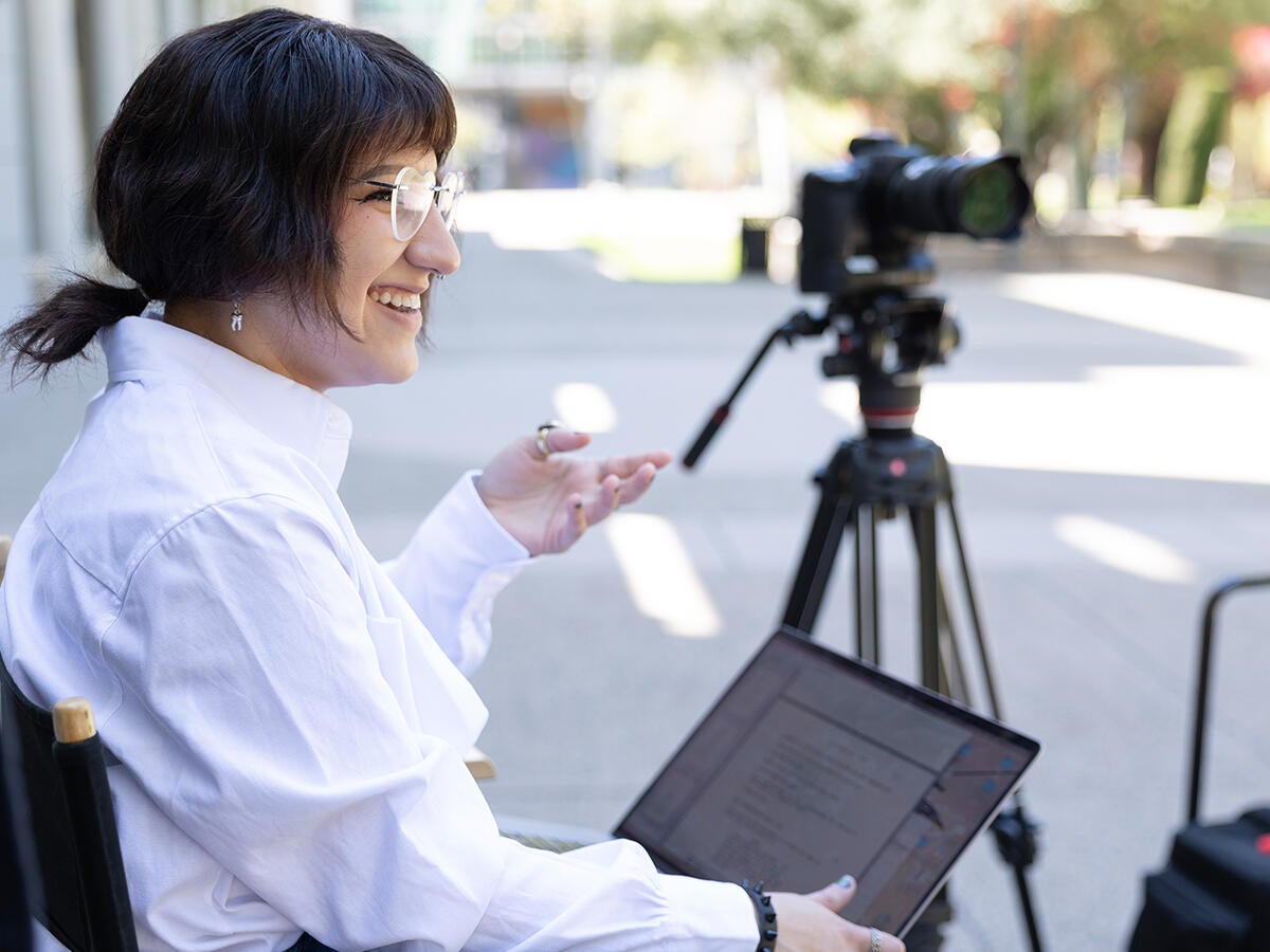 Student laughing, holding a computer with a camera behind them